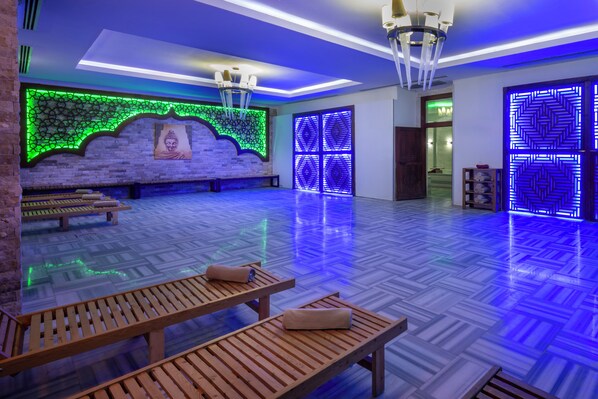 A spacious room with wooden benches, a brick wall with green LED lighting, and blue patterned walls.
