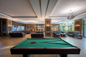 A spacious lounge area with a pool table, comfortable seating, and large windows offering a view of the outdoors. - Alan Xafira Deluxe Resort & Spa (Alanya)