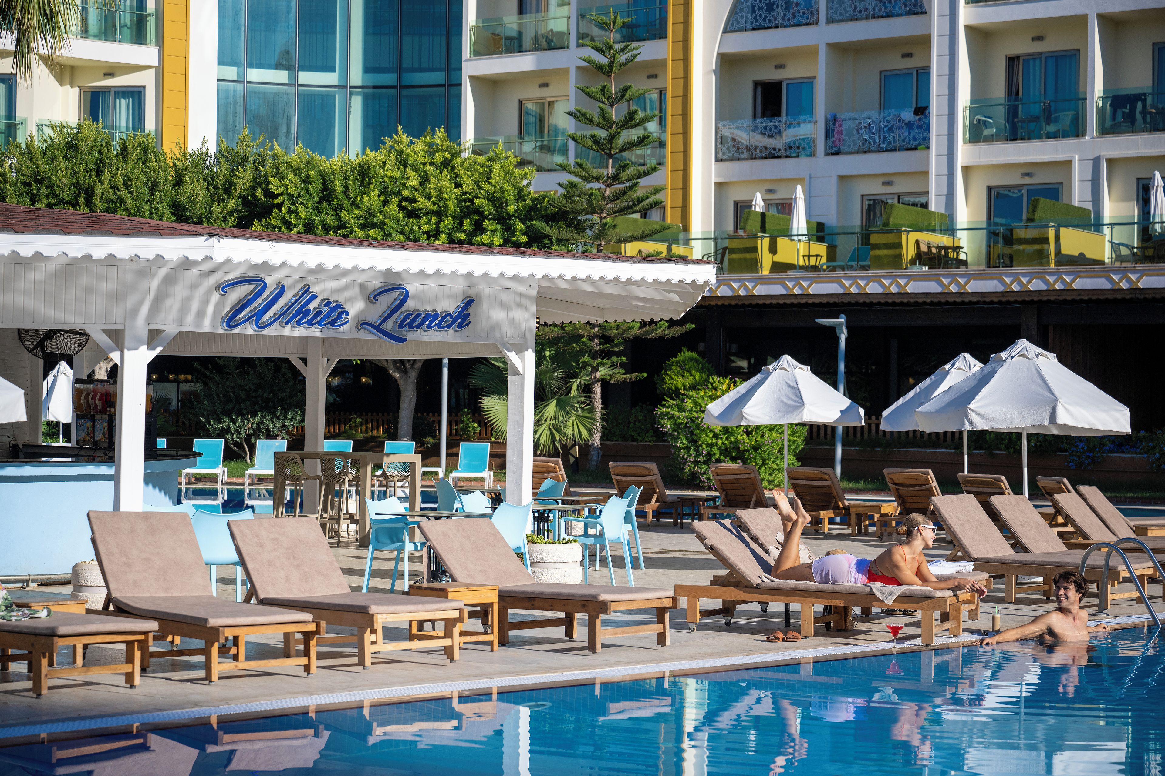 Ein Poolbereich mit Liegestühlen, Sonnenschirmen und einem Gebäude mit dem Schild "White Punch".