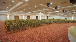A large conference room with rows of chairs, a red patterned carpet, and a high ceiling with recessed lighting. - Alan Xafira Deluxe Resort & Spa (Alanya)