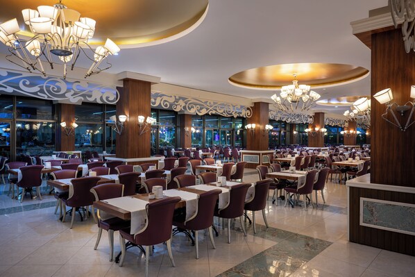A spacious restaurant with multiple tables and chairs, elegant chandeliers, and a modern interior design.