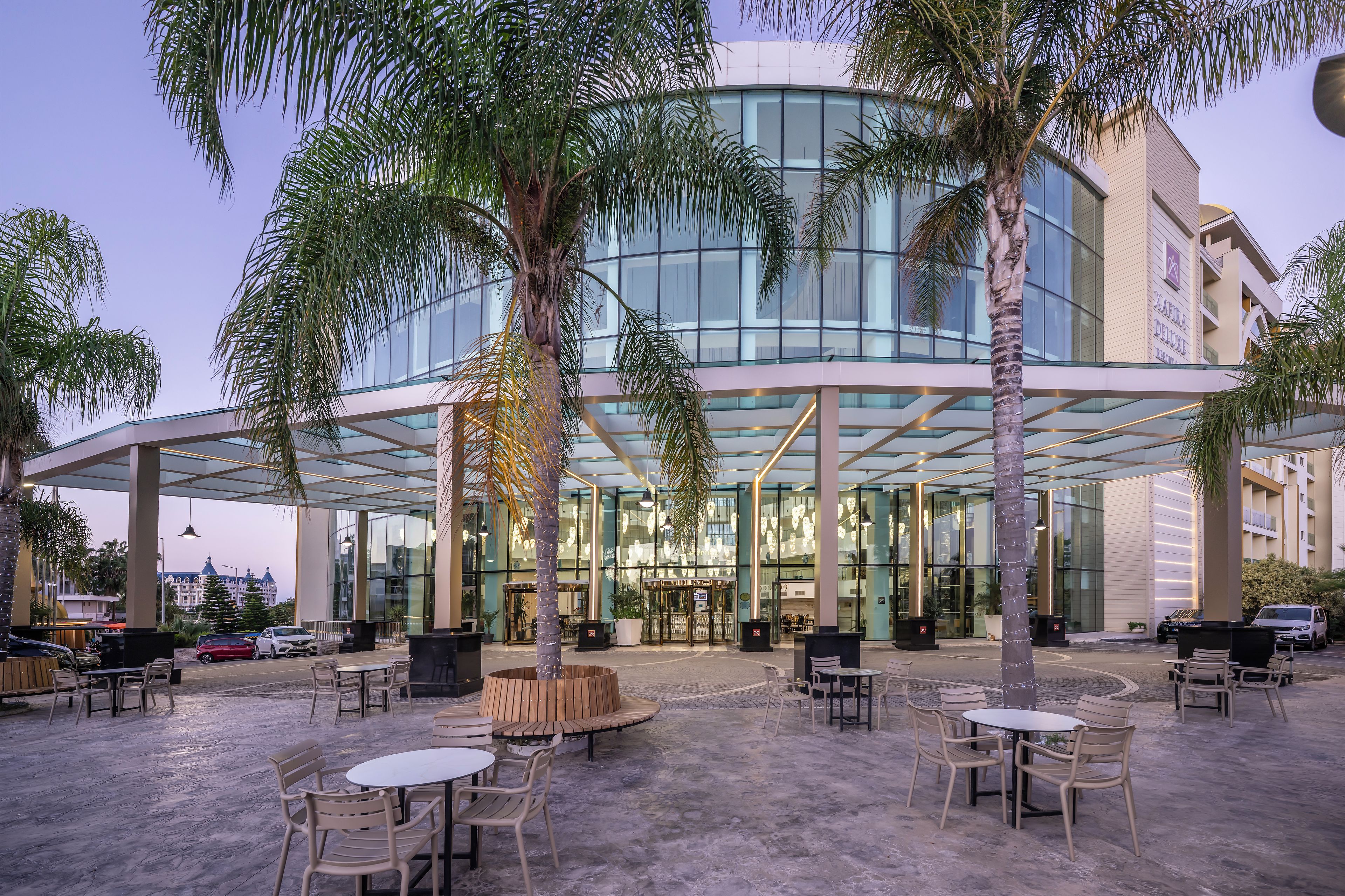 An outdoor seating area with tables and chairs, palm trees, and a modern building with glass windows.