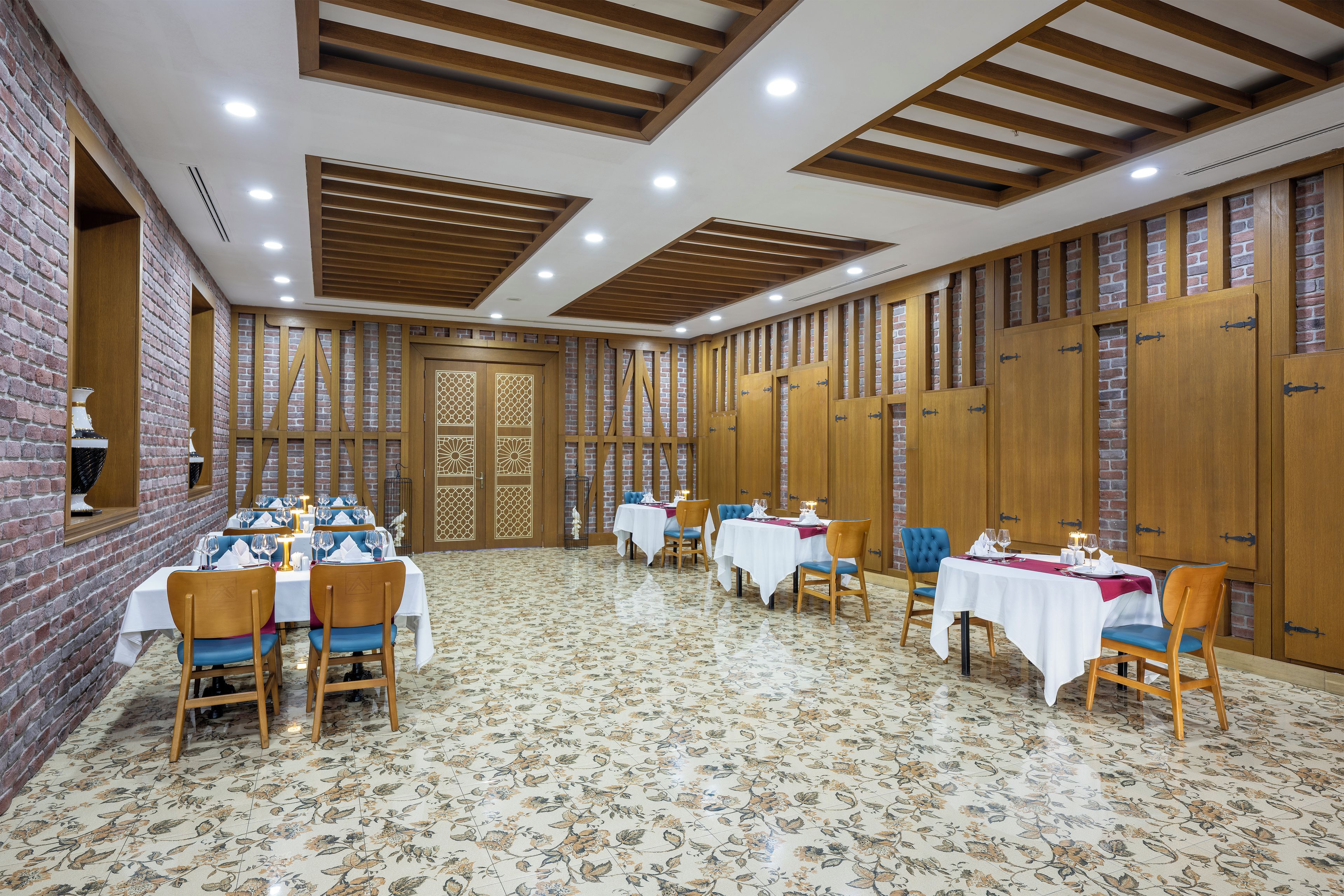 A dining area with multiple tables and chairs, wooden paneling on the walls, and a patterned floor.