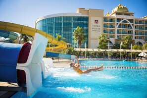 Una piscina con tobogán de agua, palmeras y un edificio hotelero con cúpula al fondo.