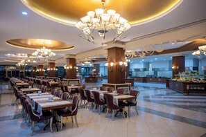 Ein geräumiges Restaurant mit mehreren Tischen und Stühlen, einer zentralen Serviettenstation und dekorativen Kronleuchtern.