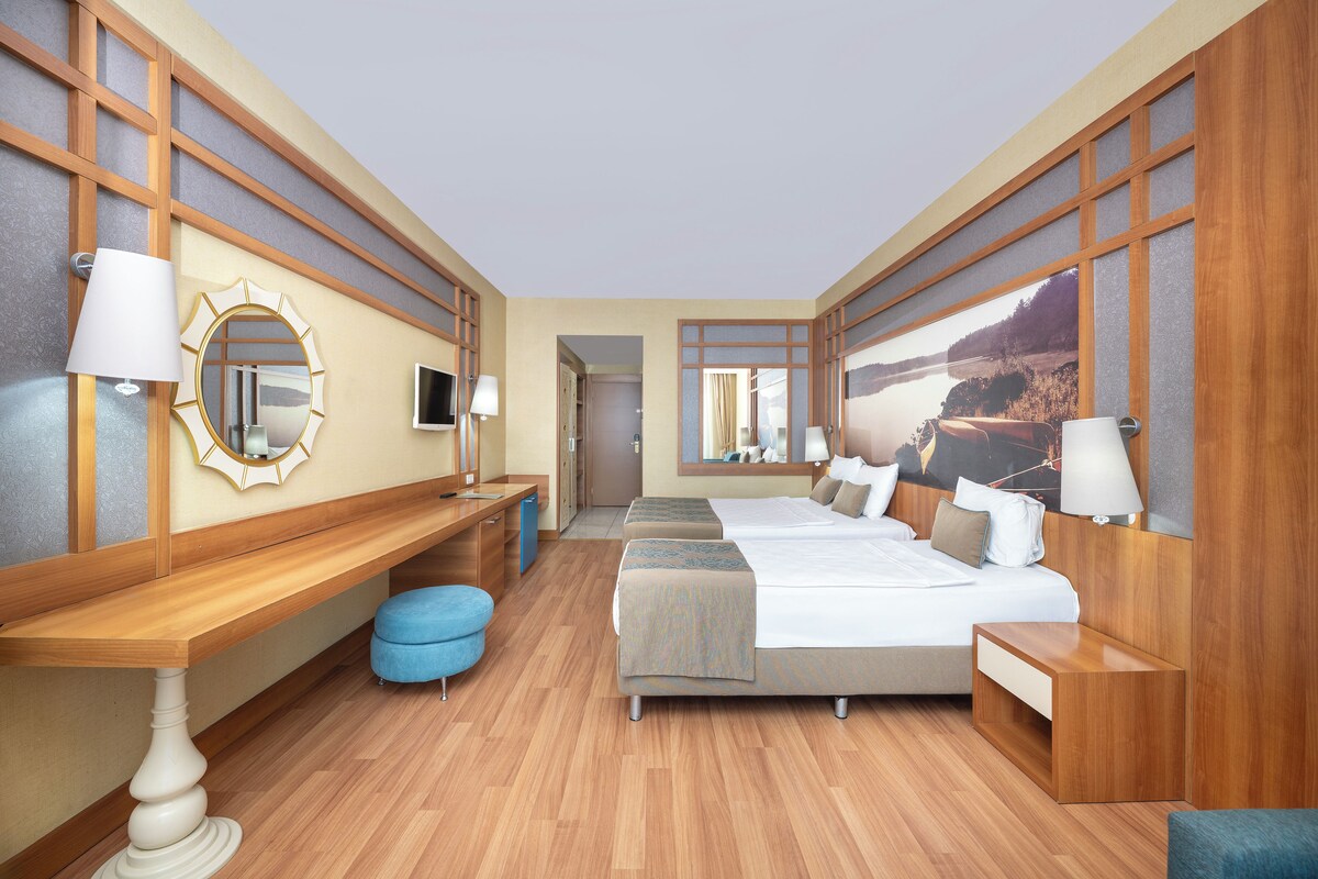 A hotel room with a large bed, a desk, a chair, a mirror, and a view of a lake.