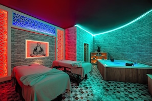 A spa room with two massage beds, a wooden bathtub, and a wall with a meditative figure. - Alan Xafira Deluxe Resort & Spa (Alanya)