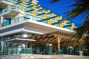 A modern hotel with multiple balconies, large windows, and a covered outdoor seating area. - Alan Xafira Deluxe Resort & Spa (Alanya)