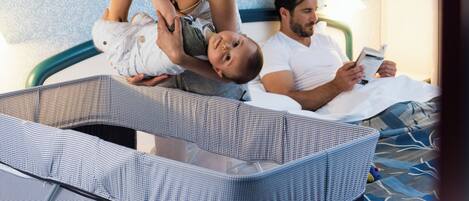 A room with a bed, a baby in a crib, and a person reading a book.