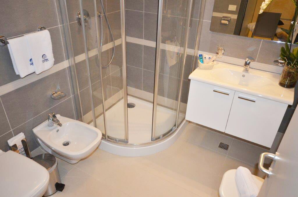 Een moderne badkamer met een douche met glazen wand, een witte wastafel en een toilet.