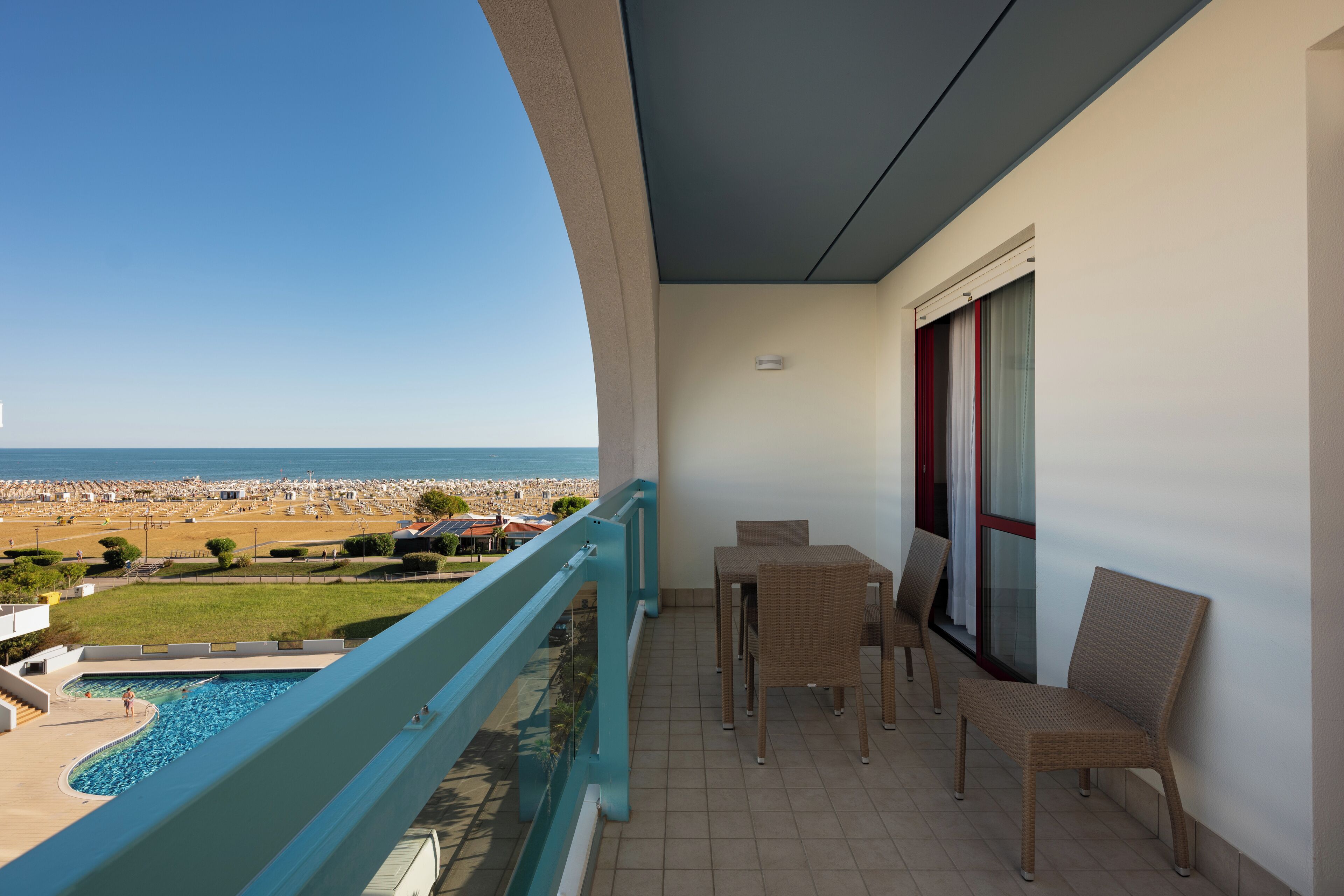 Een balkon met uitzicht op het strand, een zwembad en zitplaatsen buiten.