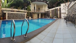 A swimming pool with metal railings, a stone wall, and a tiled patio area with outdoor furniture. - Hotel Scarlet Bukit Pakar (Bandung)