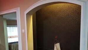 A model sailboat on a dark textured wall, a wooden bench below, and a doorway leading to another room. - Hotel Scarlet Bukit Pakar (Bandung)