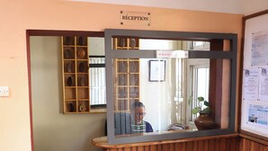 Zona de recepción con un escritorio de madera, un espejo, una silla de madera y un letrero de recepción.
