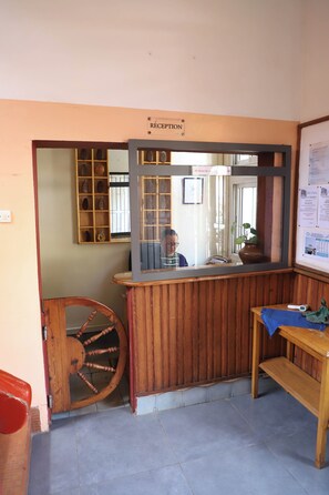 Zona de recepción con un escritorio de madera, un espejo, una silla de madera y un letrero de recepción.