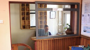 Uma área de recepção com uma mesa de madeira, um espelho, uma cadeira de madeira e a placa da recepção.