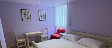 A bedroom with a bed, a desk, a chair, and a red chair.