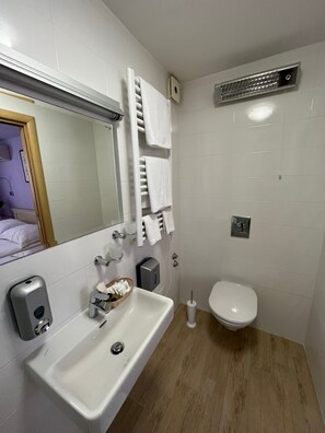 Un baño con lavamanos, inodoro, toallero y espejo.