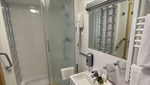 Une salle de bain moderne dotée d’une douche à parois de verre, d’un lavabo avec distributeur de savon et d’un miroir muni d’un porte-serviettes.
