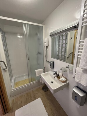 Un baño moderno con ducha de vidrio, un lavamanos con dispensador de jabón y un espejo con toallero.
