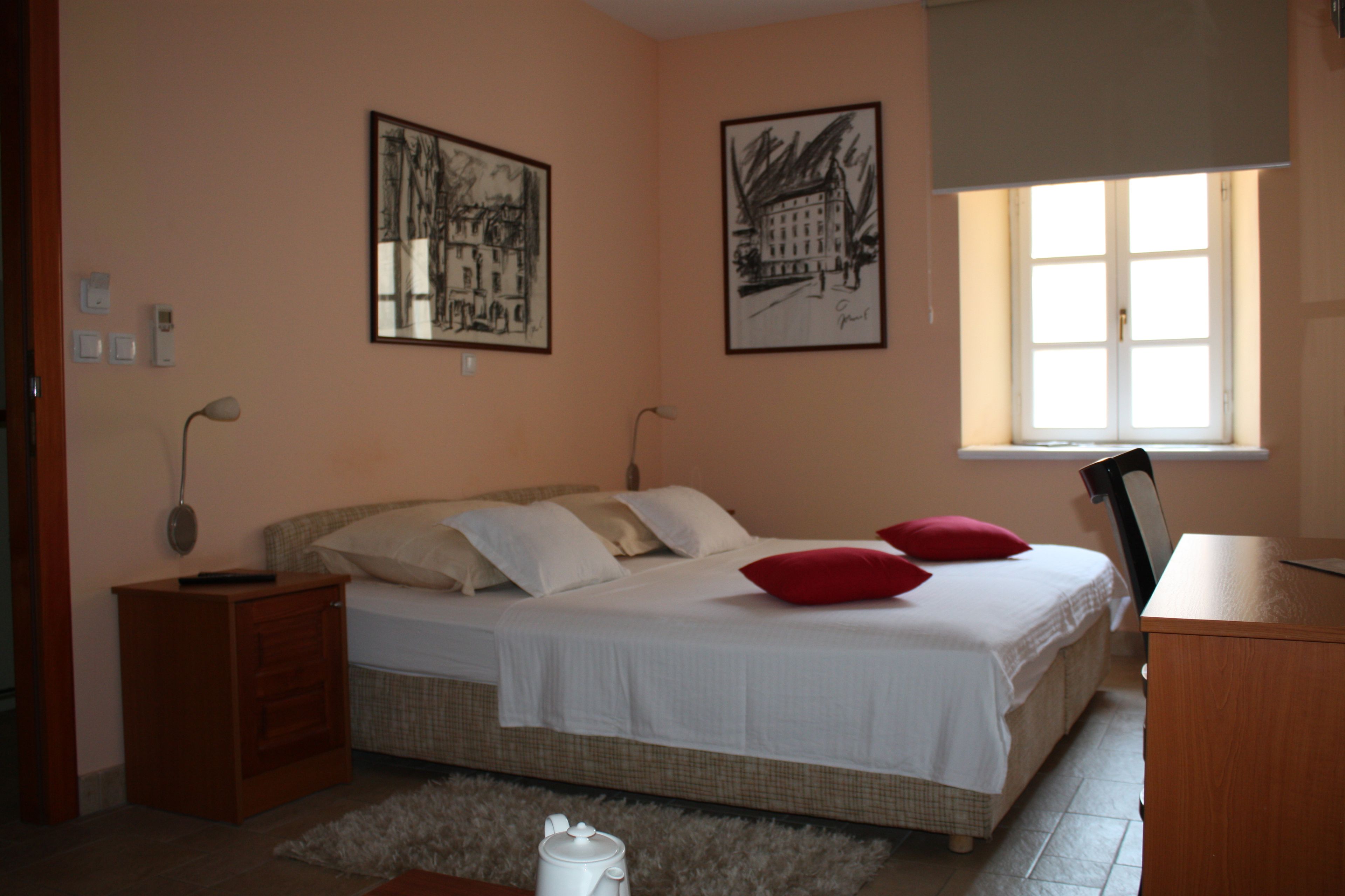 A bedroom with a bed, a nightstand, a desk, and two framed pictures on the wall.