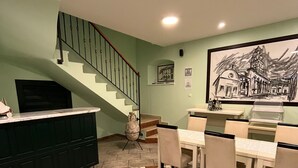 Un espace repas avec une table et des chaises, une cuisine avec un comptoir et des placards, et un escalier menant à un autre niveau.