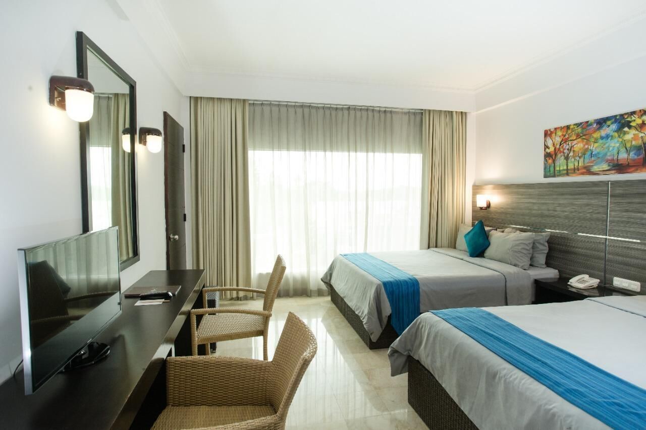 A hotel room with a bed, a desk with a chair, a television, and a painting on the wall.