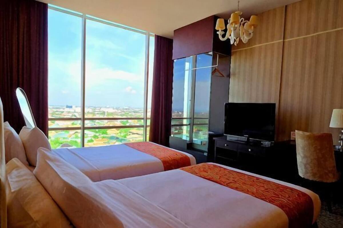 Habitación de hotel con dos camas, televisión, un ventanal y vista a la ciudad.