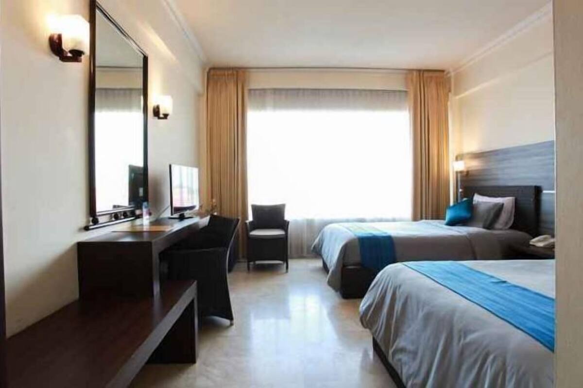 Una habitación de hotel con escritorio, dos camas, una silla y un ventanal con cortinas.