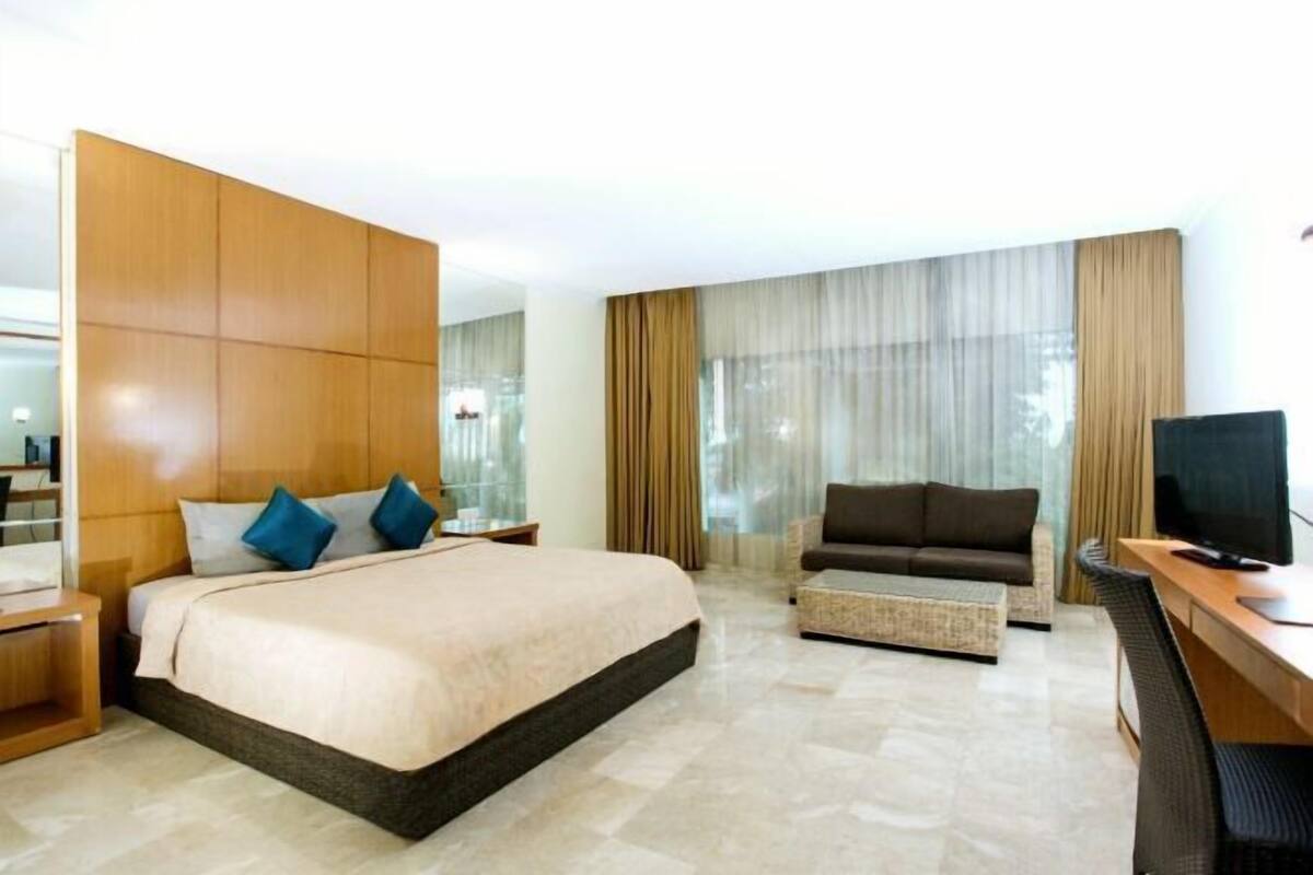 Una habitación de hotel con una cama grande, un sofá, un escritorio con una computadora y un televisor.