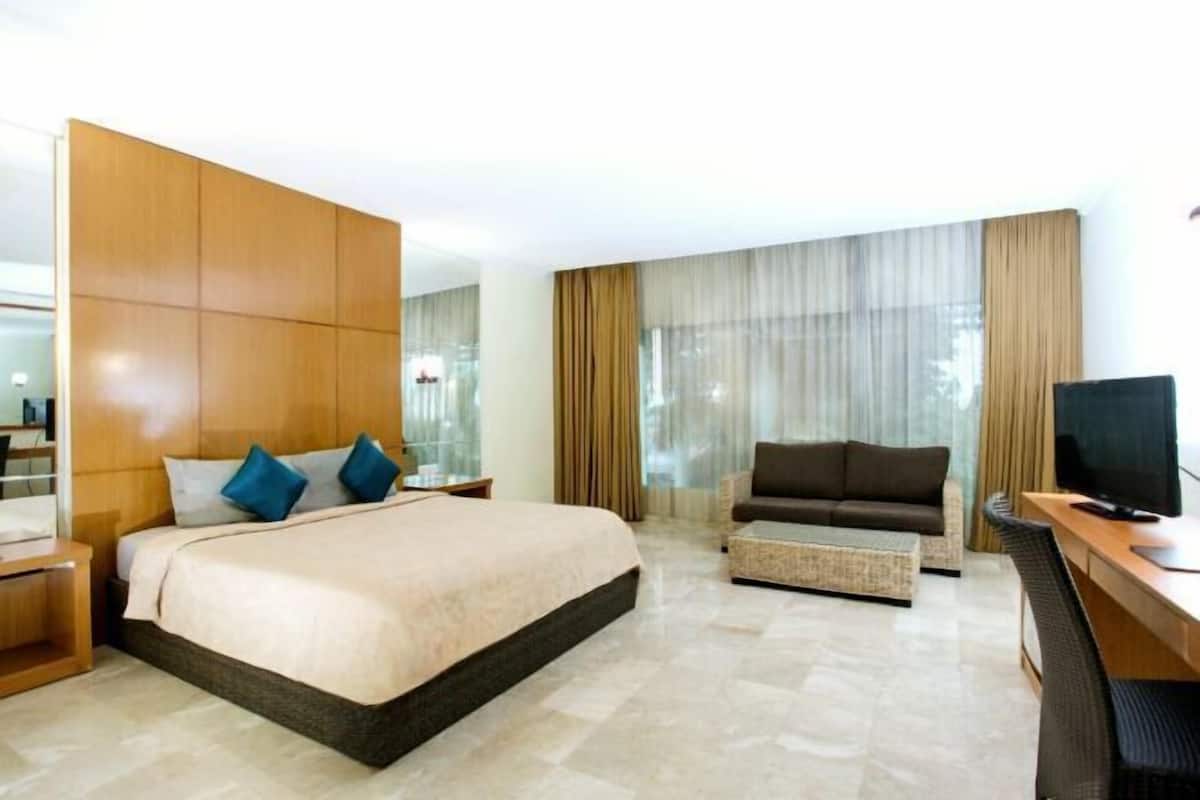 A hotel room with a large bed, a sofa, a desk with a computer, and a TV.