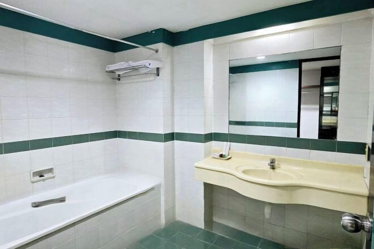 Un baño con azulejos blancos, una franja verde, una bañera, un lavabo y un espejo.