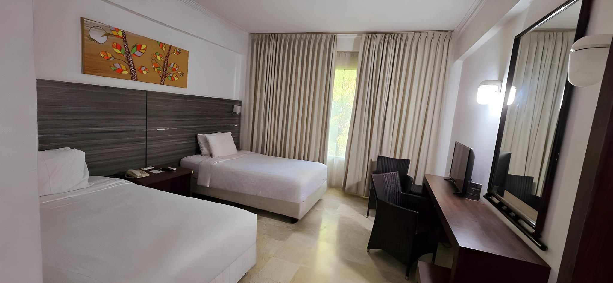 Una camera d'albergo con due letti, una scrivania, una sedia, uno specchio grande e una finestra con tende.