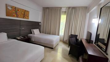 Una camera d'albergo con due letti, una scrivania, una sedia, uno specchio grande e una finestra con tende.