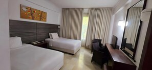 Une chambre d’hôtel avec deux lits, un bureau, une chaise, un grand miroir et une fenêtre avec des rideaux.