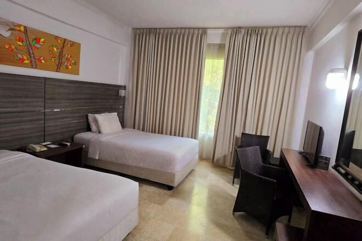 Habitación de hotel con dos camas, un escritorio, una silla, un televisor y un ventanal con cortinas.