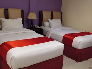 A hotel room with two beds, a nightstand, and a lamp.