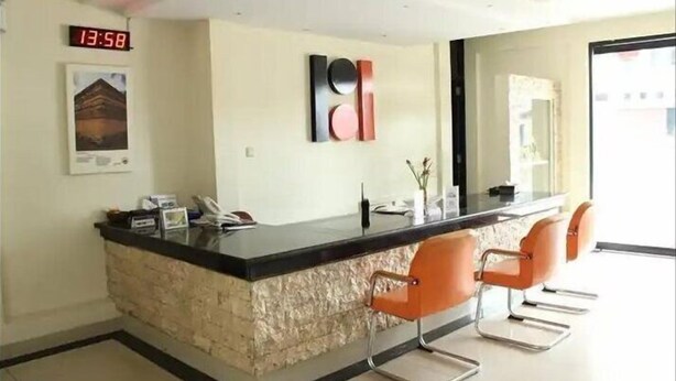 A reception area with a stone counter, two orange chairs, a digital clock, and a framed picture on the wall. - Pundi Rejeki Hotel (Jambi)