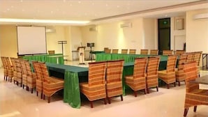 A conference room with a long table, chairs, a projector screen, and a podium. - Pundi Rejeki Hotel (Jambi)