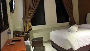 A hotel room with a bed, a small table with a remote control, a chair, and a window with curtains. - Pundi Rejeki Hotel (Jambi)