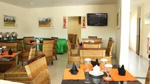 A dining area with wicker furniture, tables set with orange placemats, and a flat-screen TV mounted on the wall. - Pundi Rejeki Hotel (Jambi)