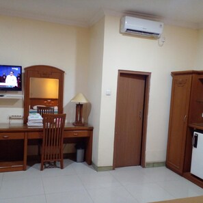 Una habitación con un escritorio de madera, una silla, una lámpara, un televisor, aire acondicionado y un armario.