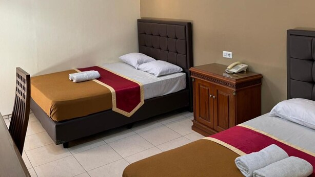 A hotel room with two beds, a wooden nightstand with a phone, and a chair. - Hotel Priangan (North Cirebon)