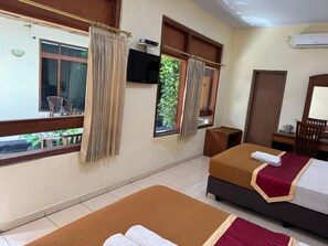 A hotel room with two beds, a television, a desk with a chair, and windows with curtains. - Hotel Priangan (North Cirebon)