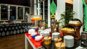 A buffet setup with various dishes, a water dispenser, and a seating area with a chair and table. - The Rizen Hotel (Cisarua)