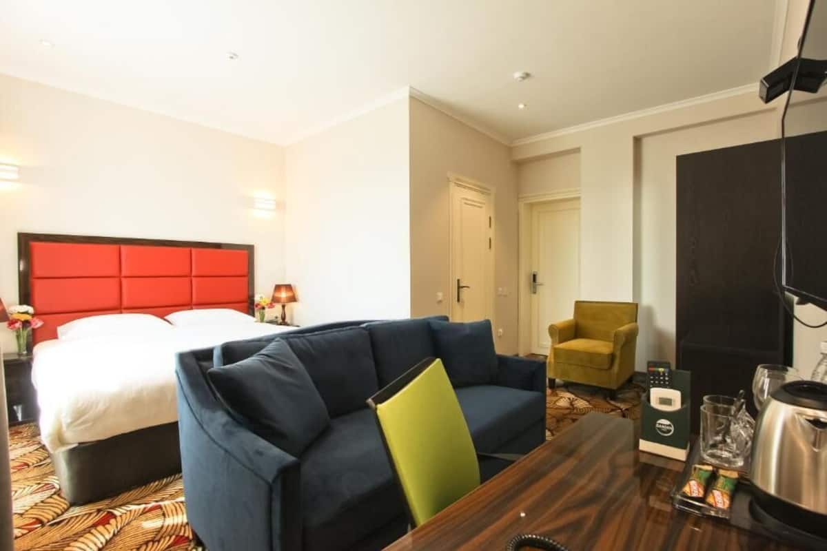 Una habitación de hotel con cama, sofá azul, mesa de madera, una silla, televisor y puerta.