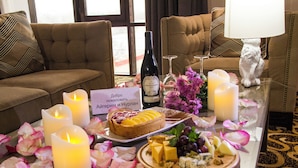 Ett bord med ljus, en vinflaska, en efterrätt, ost och blommor, placerat i ett rum med en soffa och en dekorativ kattstaty.