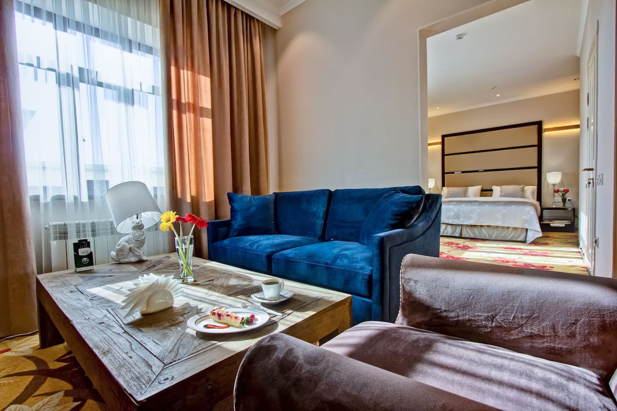 Ein Hotelzimmer mit einem blauen Sofa, einem Holztisch mit einer Speisenplatte, einer weißen Lampe und einem Bett mit weißer Bettwäsche.