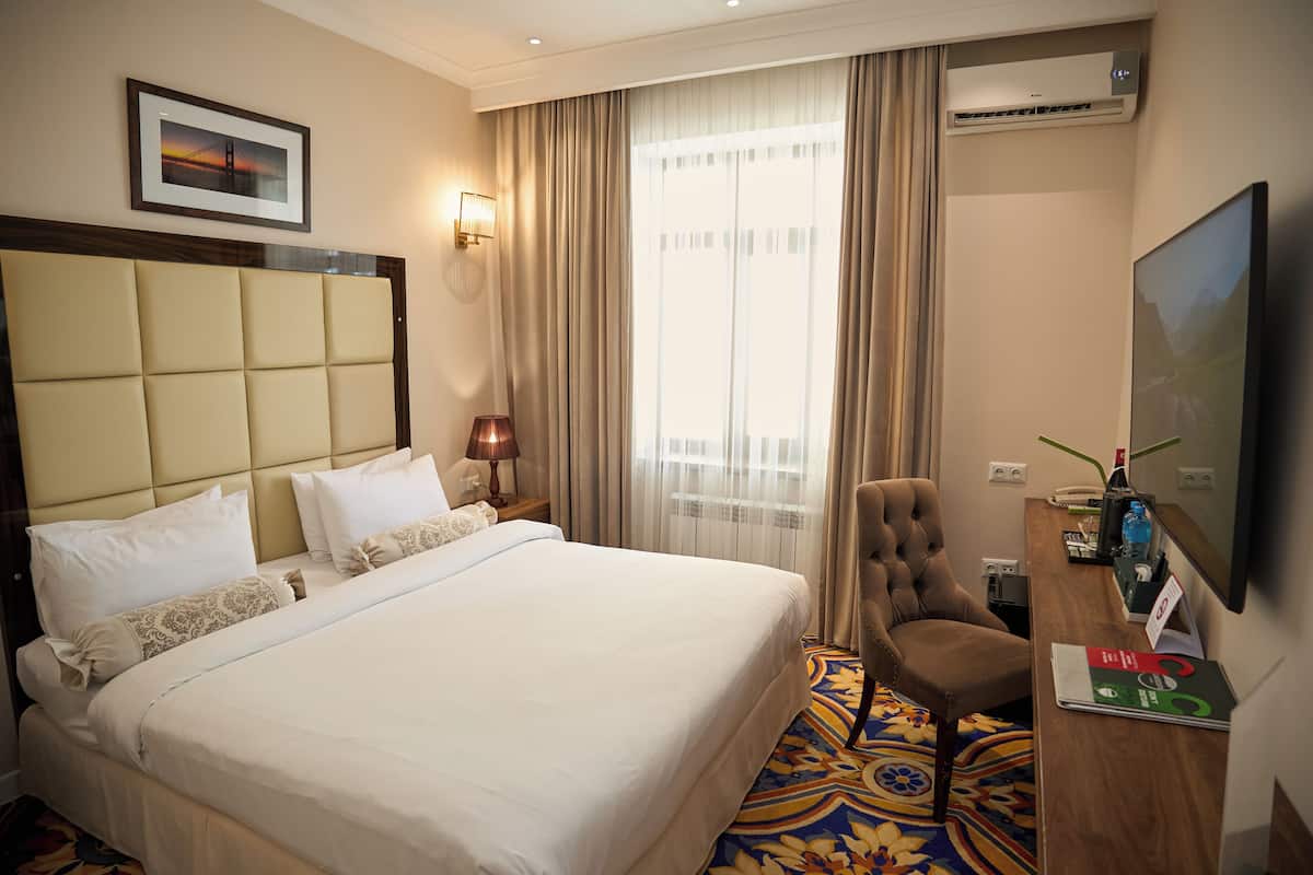 Ein Hotelzimmer mit einem großen Bett, einem Schreibtisch mit Stuhl, einem Fernseher und einer Klimaanlage.