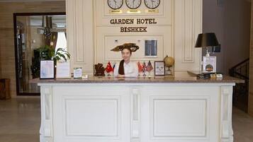 A reception desk with clocks displaying Moscow, Bishkek, and Beijing times, a sign for Garden Hotel Bishkek, and various flags.